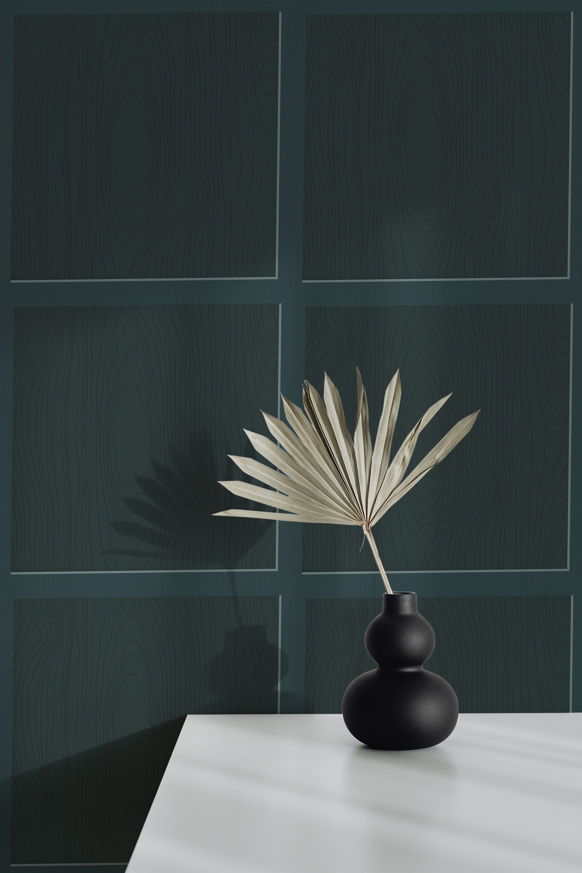 Self-adhesive dark green geometric-patterned wallpaper on a room wall with a decorative vase and dried plant on a white surface.