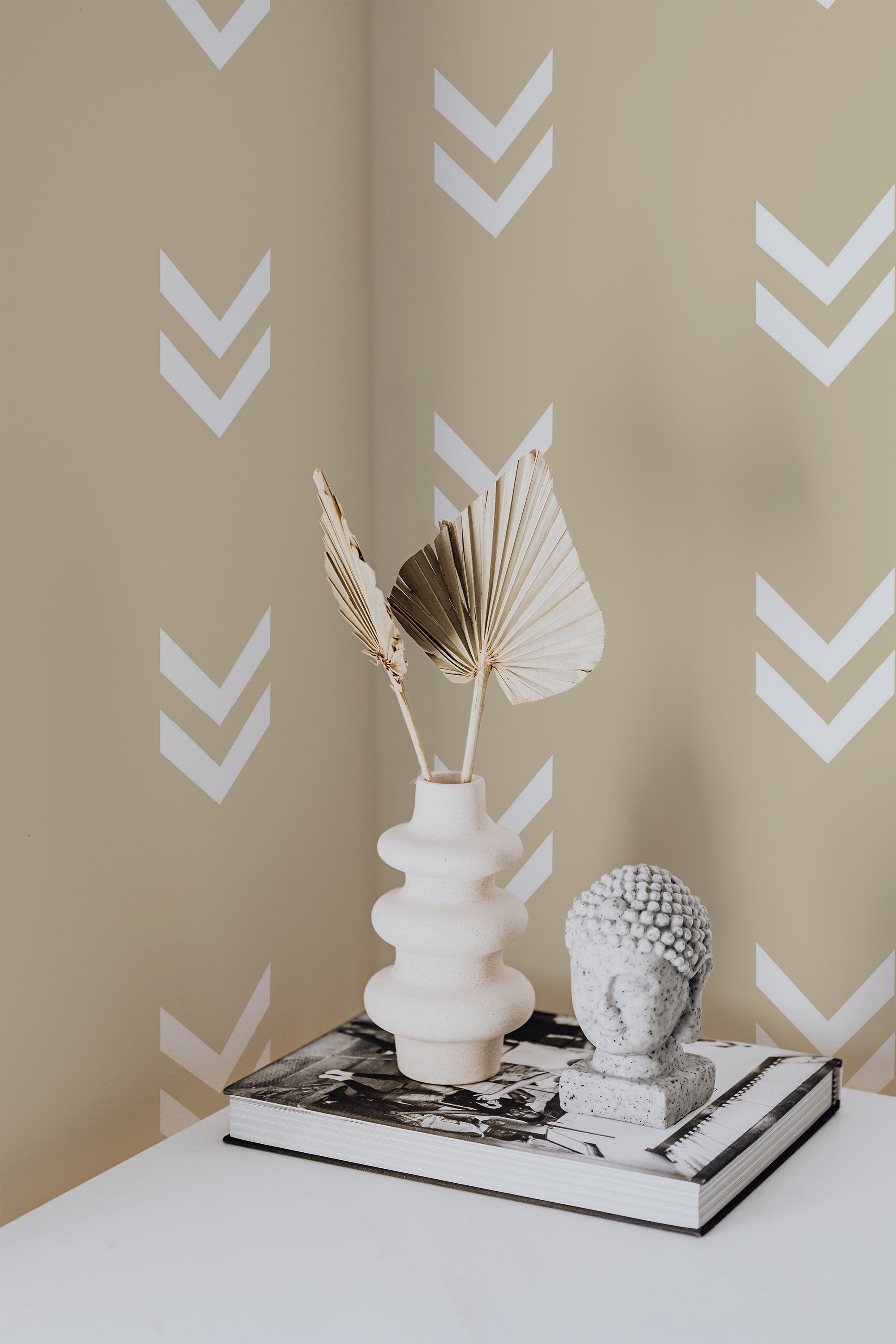 Self-adhesive wallpaper with a minimal chevron pattern in white over a pale green background, shown in a room with decorative items on a table.