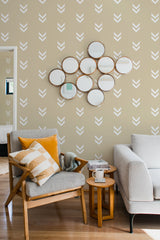 A cozy room with tan walls adorned with a minimal chevron pattern in white. A grouping of circular mirrors adds a decorative touch above a chair with yellow accents. Traditional wallpaper.