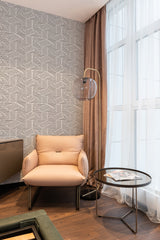 A clean and well-lit room with a striking striped triangle wallpaper pattern covering one wall, complemented by sheer curtains, a tan armchair, and traditional decor. Traditional wallpaper.
