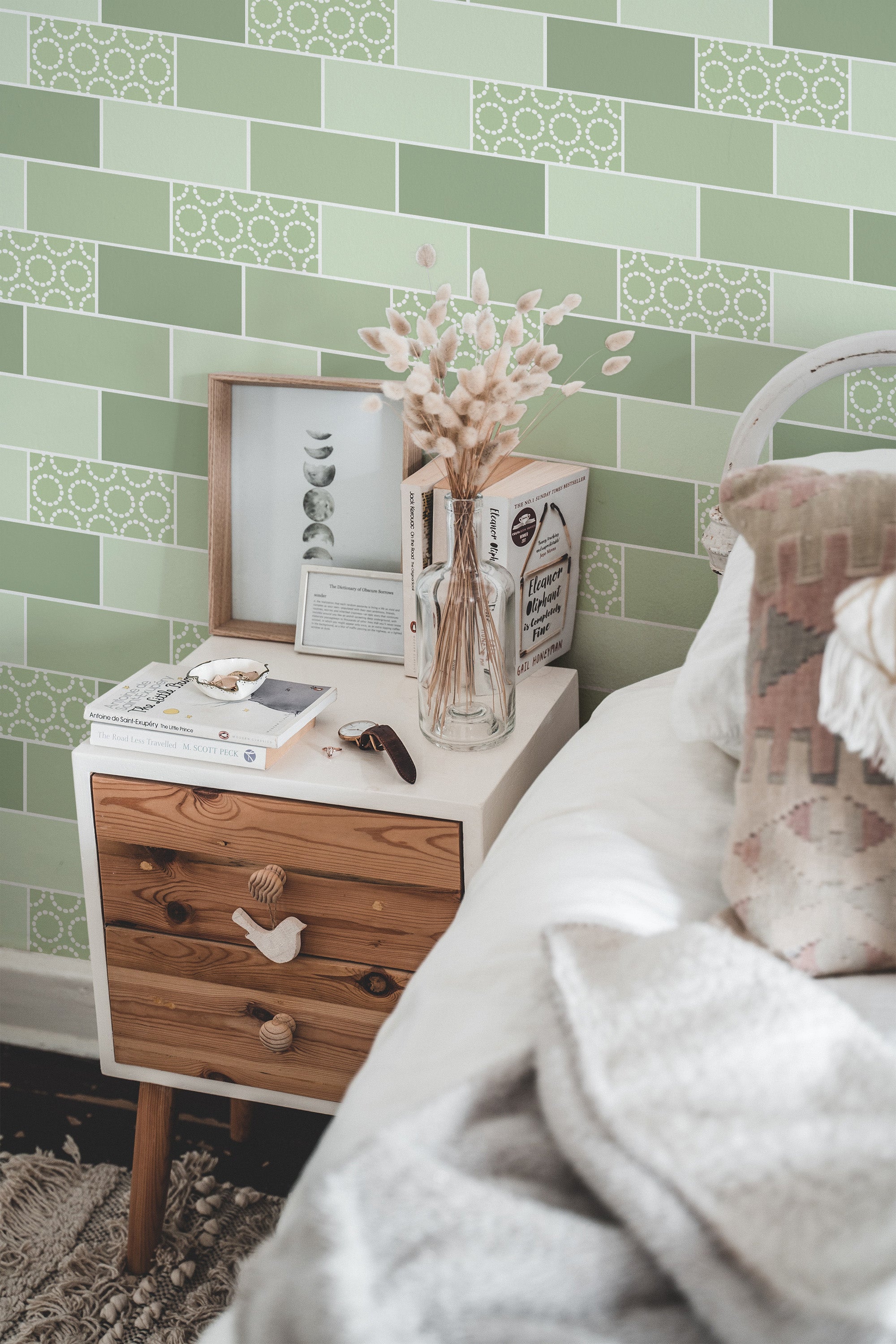 Self-adhesive green tile-patterned wallpaper with a geometric design on a bedroom wall, complementing a wooden bedside table and cozy bedding.