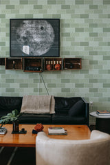A living room with a green tile-designed wallpaper, including a repeating pattern of lighter green squares outlined in white, accented with geometric shapes, giving a contemporary twist to traditional wallpaper.
