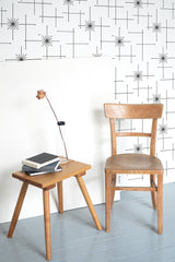 Self-adhesive wallpaper with a seamless star pattern on a light wall, beside a wooden chair and table with a lamp and books.