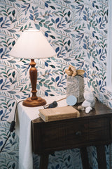 Self-adhesive blue watercolor leaf wallpaper in a room with a wooden table, lamp, and decorative items.