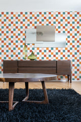 A room with colorful check-patterned wallpaper in shades of orange, green, and white, above a wooden credenza with a mirror and vases, ending with a shaggy black rug, traditional wallpaper.