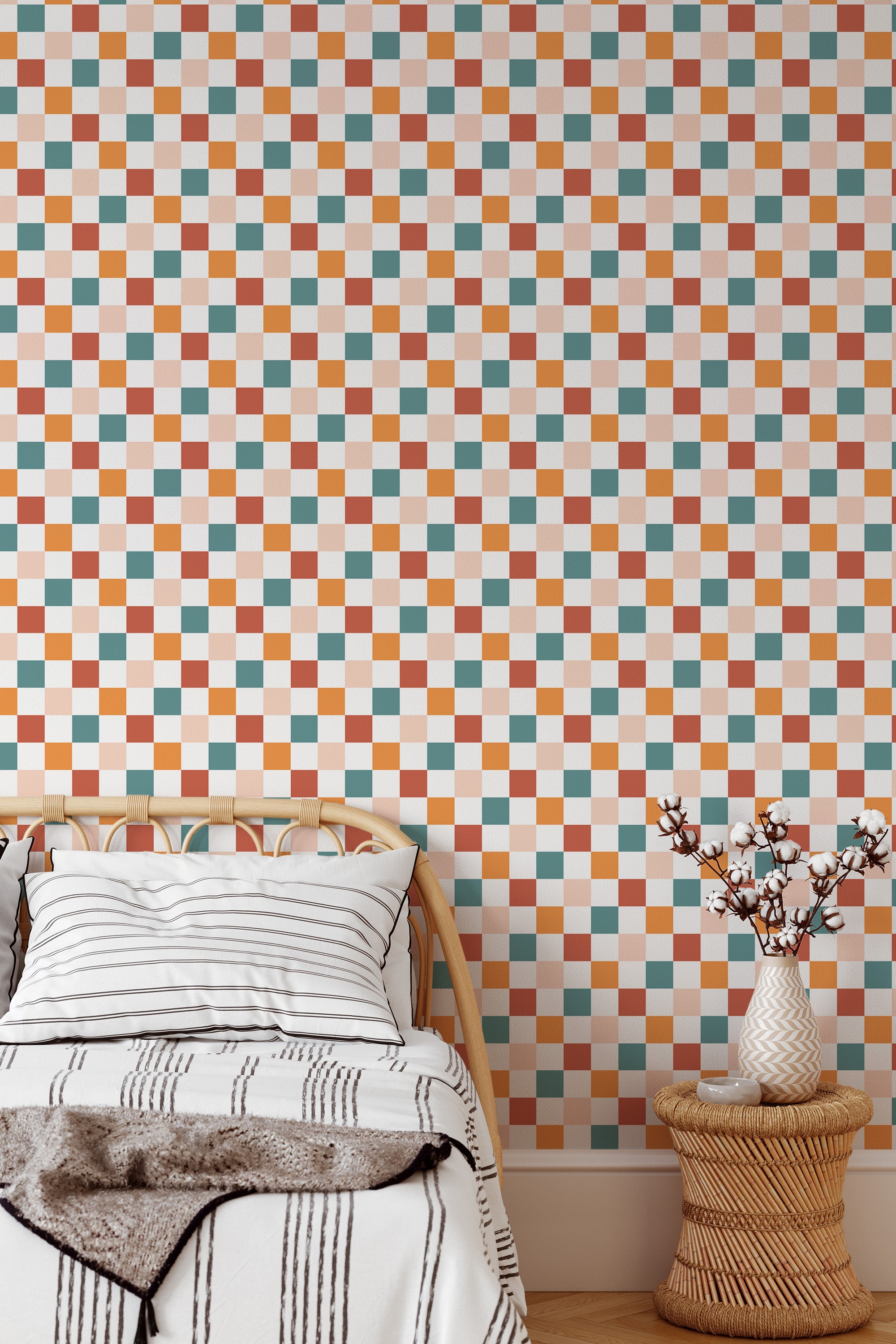 Self-adhesive wallpaper with a colorful checkered pattern in shades of peach, white, and beige, covering a bedroom wall above a wooden bed and beside a vase of flowers on a stool.
