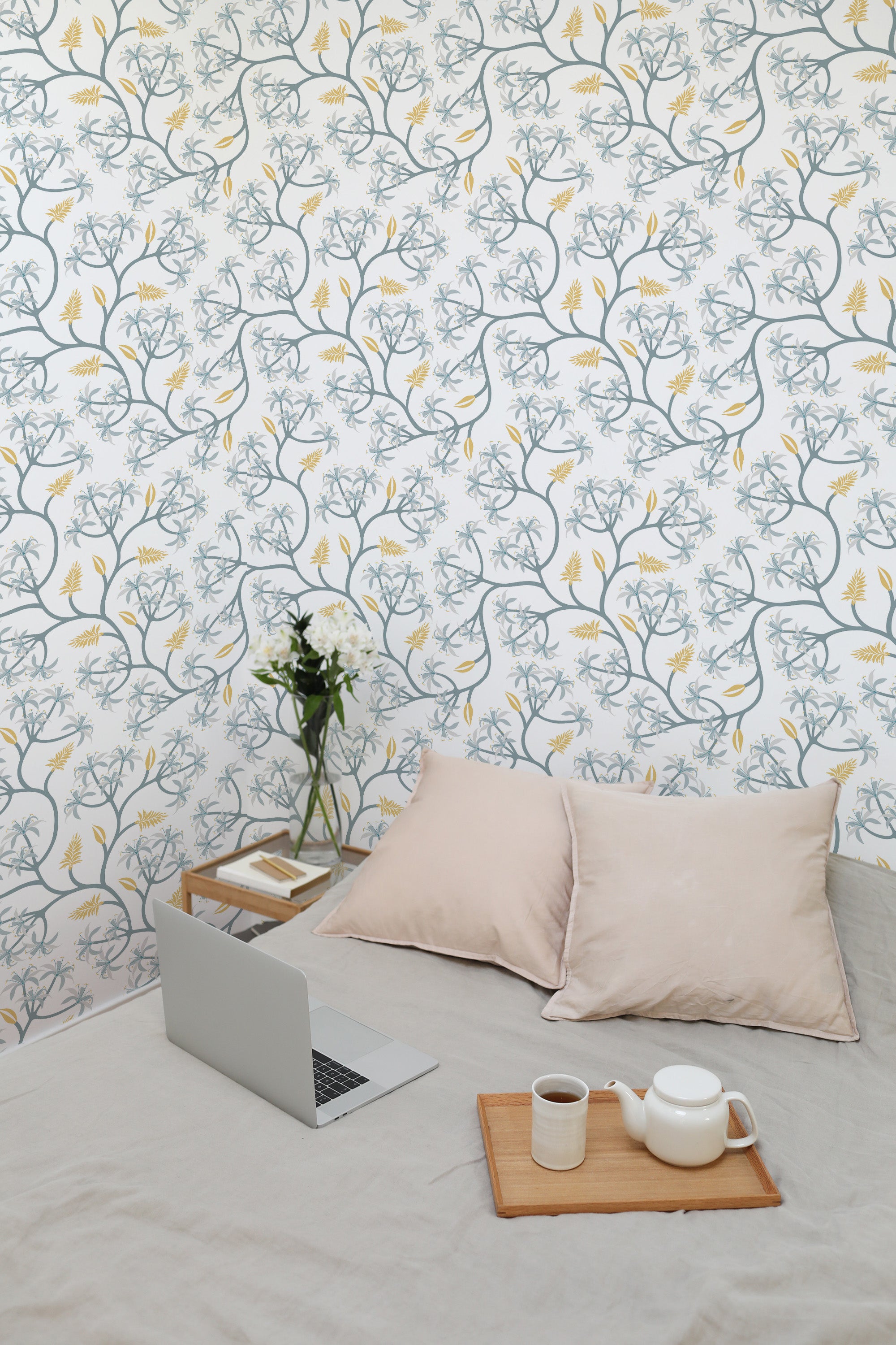 Self-adhesive blue floral wallpaper with seamless botanical pattern adorning a room's wall, complemented by soft furnishings and a laptop on a bed.