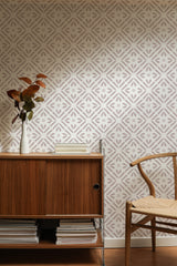Self-adhesive wallpaper with geometric star-like patterns in neutral tones on an interior wall, complementing wooden furniture and a vase with dried leaves.