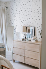 A room with white and gray star-patterned wallpaper on one wall, adding a whimsical touch to the space. Includes a wooden dresser and a table lamp. Traditional wallpaper.
