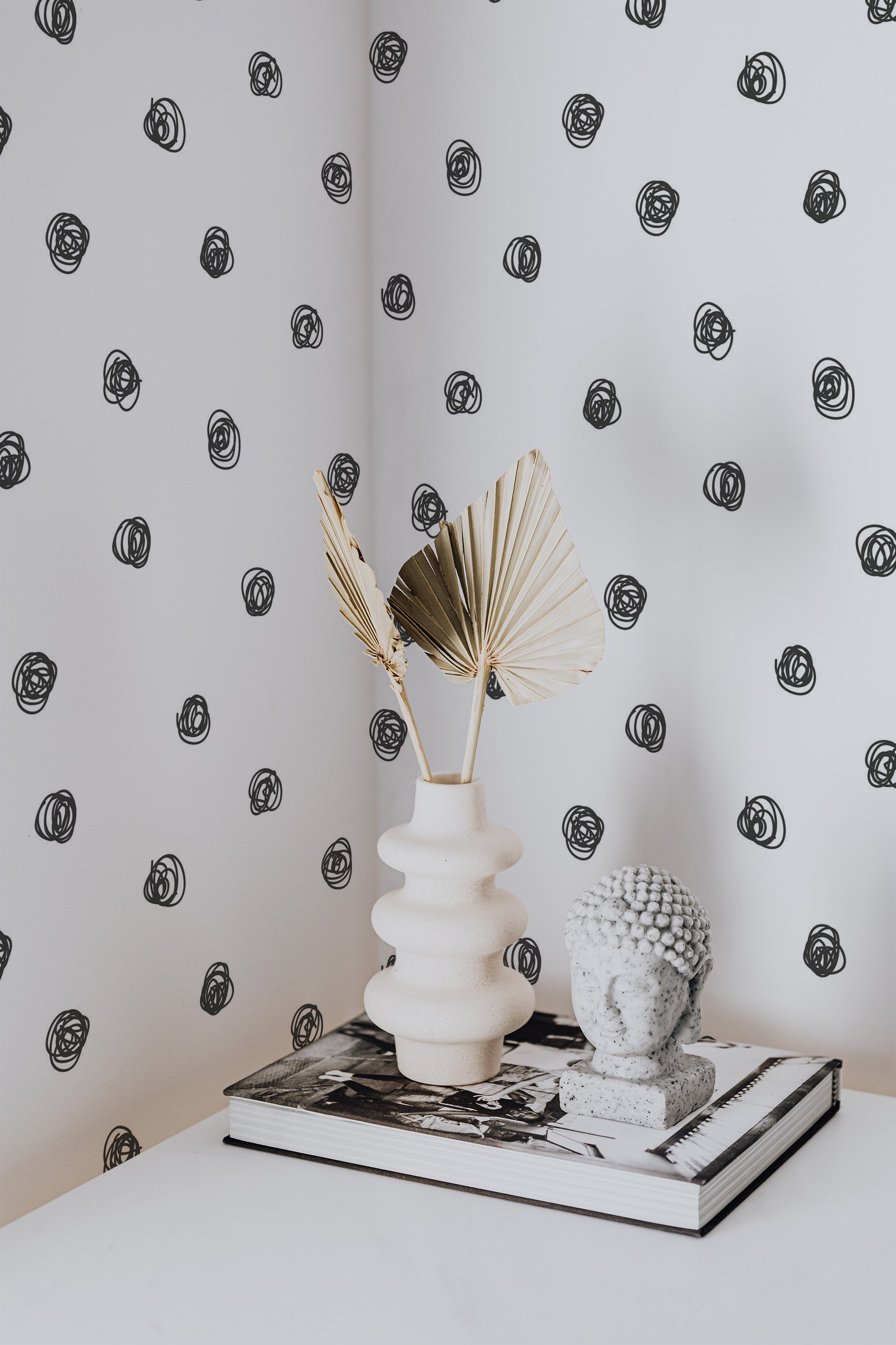 Self-adhesive wallpaper with black hand-drawn dots pattern on a white background, with a decorative vase and sculpture on a book in the foreground.