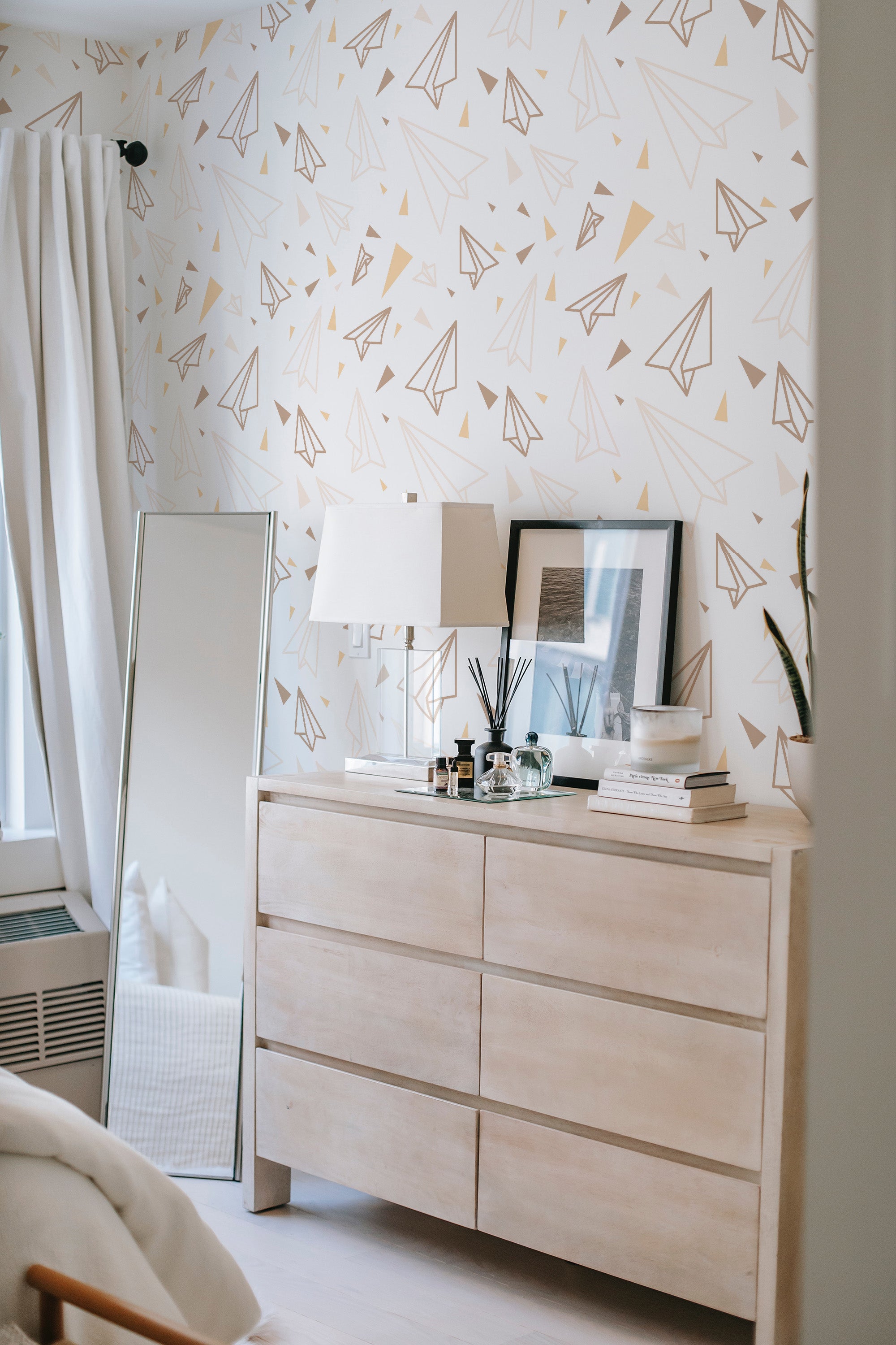 A room with a wall covered in paper plane patterned wallpaper in pastel shades, adding a playful and modern twist to traditional wallpaper.