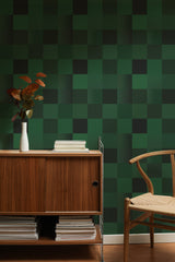Self-adhesive dark green tile pattern wallpaper in a room with a wooden sideboard and chair, and decorative plant on top.