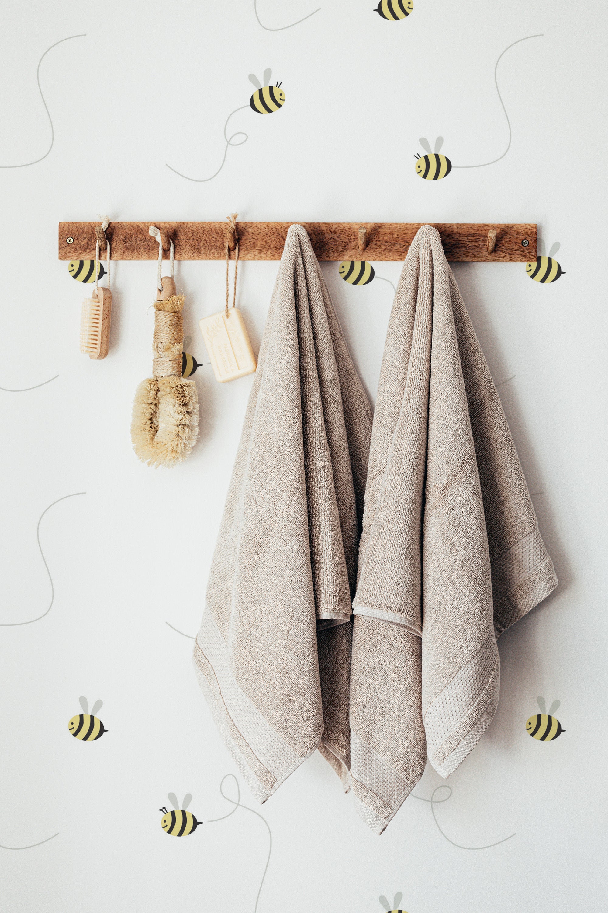 Self-adhesive wallpaper with a bee line pattern, including small bee illustrations and curved lines, complementing the neutral-toned towels hanging on a wooden rack.