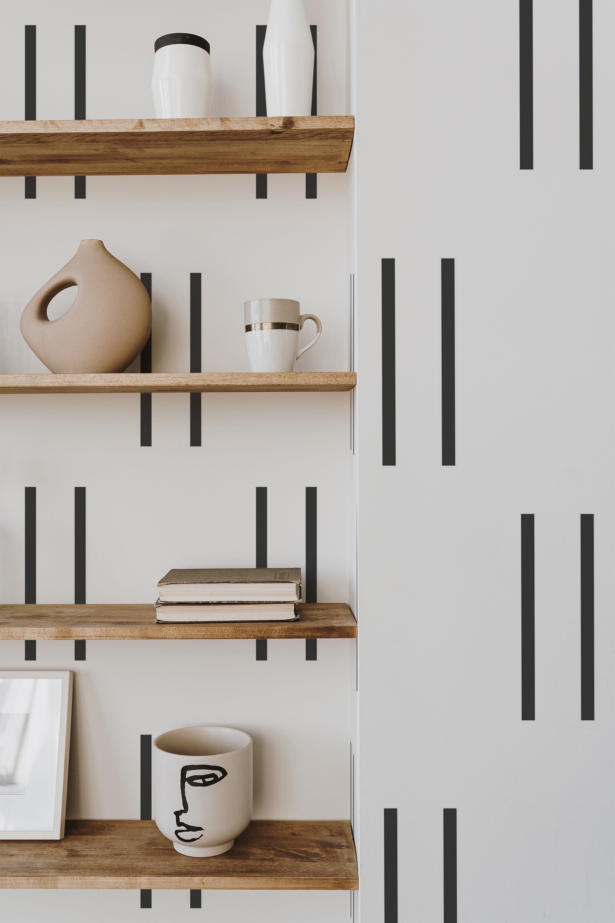 Self-adhesive wallpaper with vertical black stripes on a white background, alongside wooden shelves with decorative items.