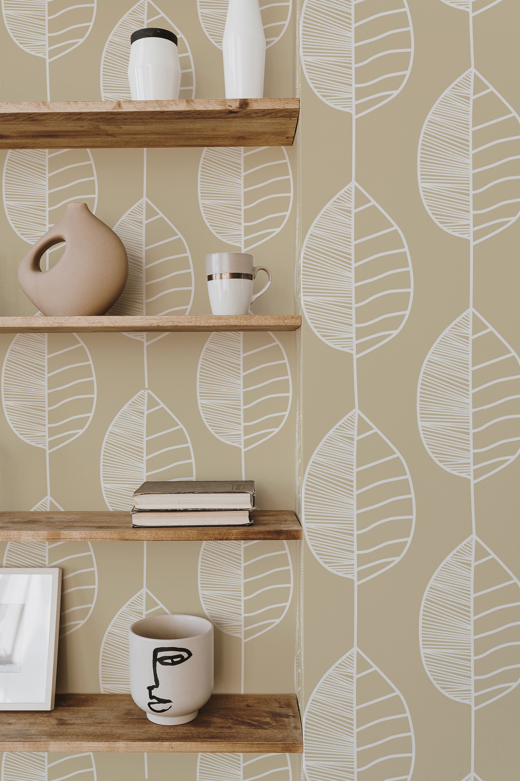 Self-adhesive wallpaper with white line art of leaves on a muted yellow background, complementing wooden shelves with assorted decorative items.