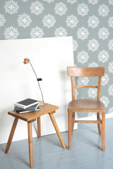 Self-adhesive retro ornamental wallpaper with white floral patterns on a soft blue background in a room with a wooden chair and stool.