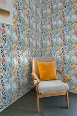 A room with a corner wall covered in Spring-themed wallpaper with a pattern of stylized flowers and leaves in shades of orange, blue, and gray, accompanied by an armchair with a yellow cushion, completing a bright, traditional wallpaper setting.