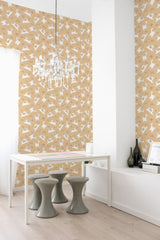 A room with a wall covered in beige wallpaper with a pattern of stylized white cats in various poses, complemented by a modern white desk, stools, and chandelier, embodying a traditional wallpaper style.