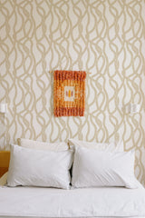 Self-adhesive wallpaper with a leaf stripe pattern in a soft beige color on a white bedroom wall above a bed with white pillows.