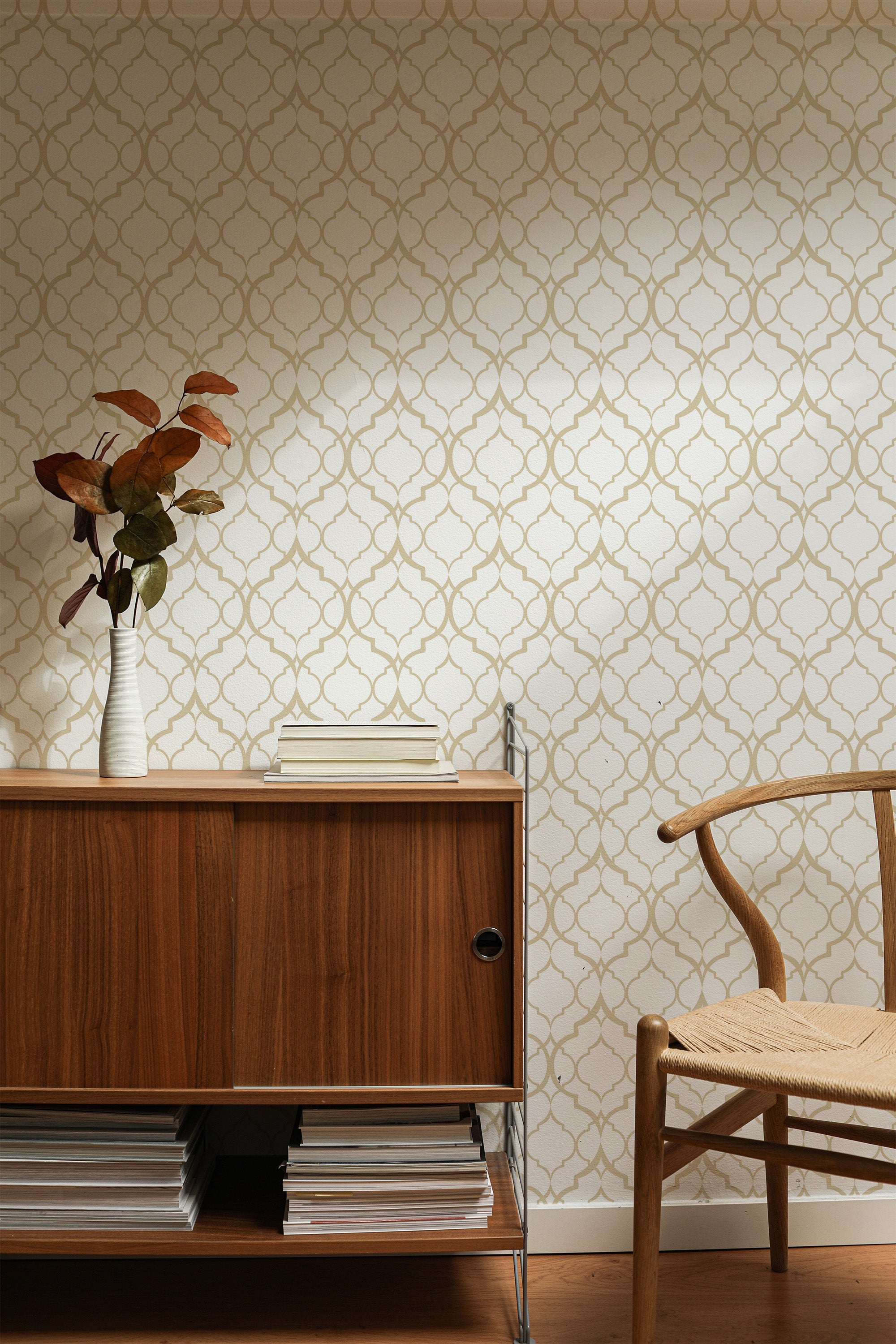 Self-adhesive wallpaper with a repeating chain pattern in neutral tones on a room wall, complemented by wooden furniture.