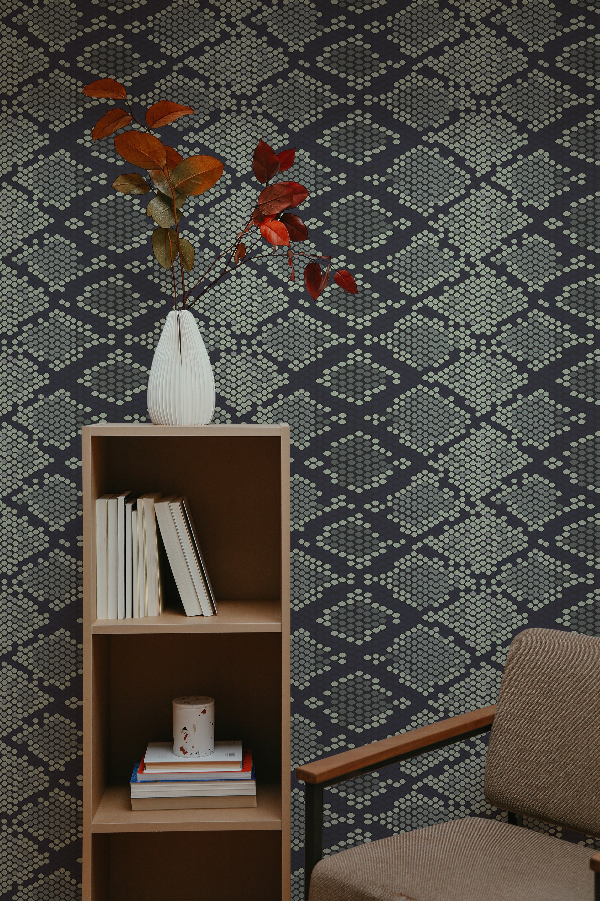Self-adhesive dark snake skin patterned wallpaper with geometric scales in a room, accompanied by a wooden bookshelf, a vase with red leaves, and a brown armchair.