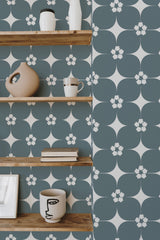 Self-adhesive Mid-century floral wallpaper with teal background and white stylized flowers, accentuated with small pink blossoms and dark green leaves.
