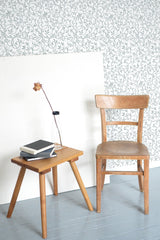 Self-adhesive wallpaper with intricate repeating ornamental pattern, complementing a wooden chair and table set in a room.