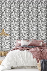 A bedroom with a wall covered in bamboo tree patterned wallpaper, in black and white, behind a bed with rose-colored bedding, traditional wallpaper.