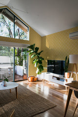 A bright room with mid-century modern furniture and a wall adorned with yellow retro square patterns, comprising repetitive geometric shapes in a vibrant, sun-kissed hue. Traditional wallpaper.