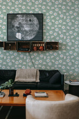 A room with green wallpaper adorned with small white daisies and yellow centers in a repeating pattern, giving the space a vintage and fresh ambiance. The wallpaper is traditional.