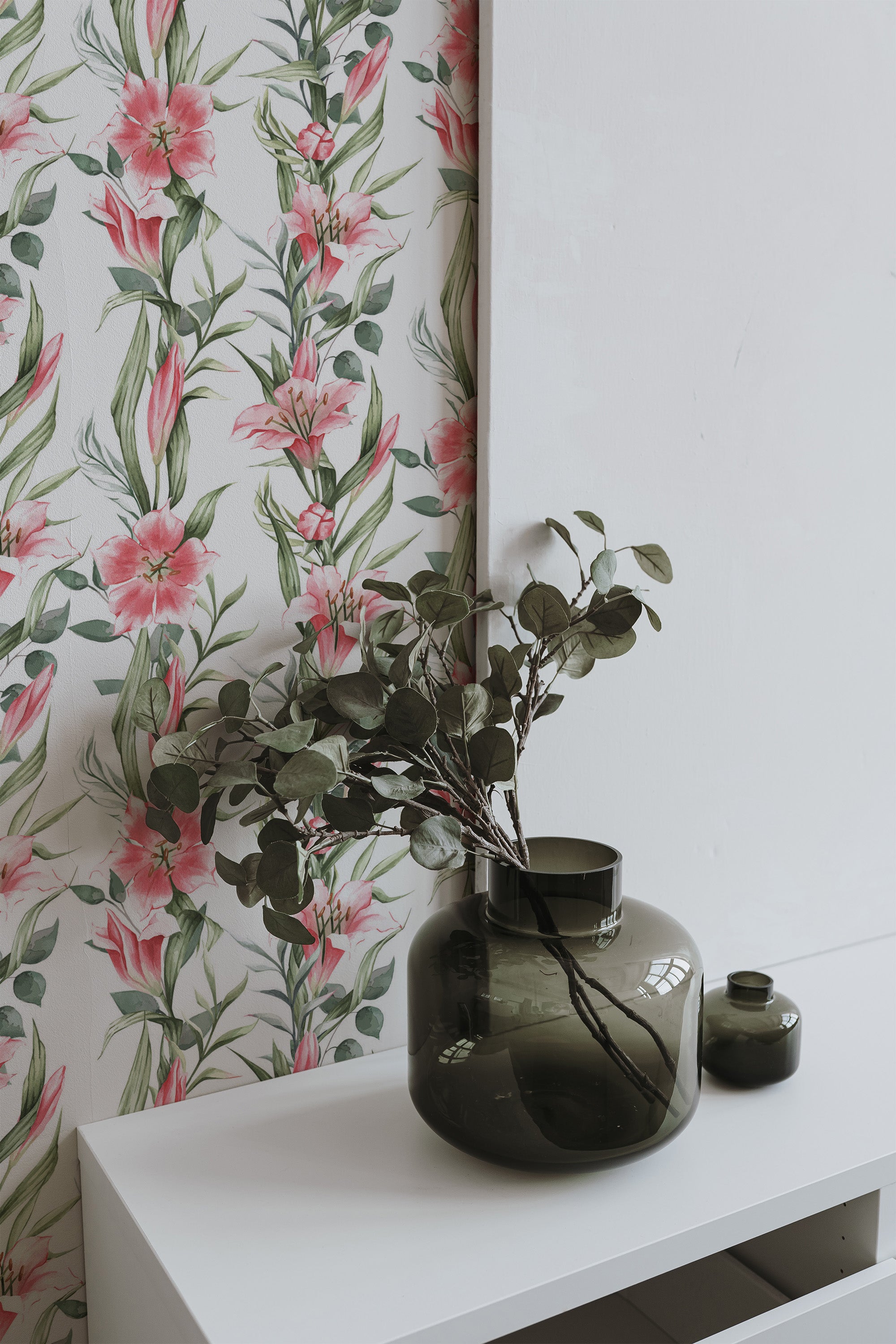 Self-adhesive wallpaper with a floral design of pink lilies intertwined with green leaves, set against a white background.