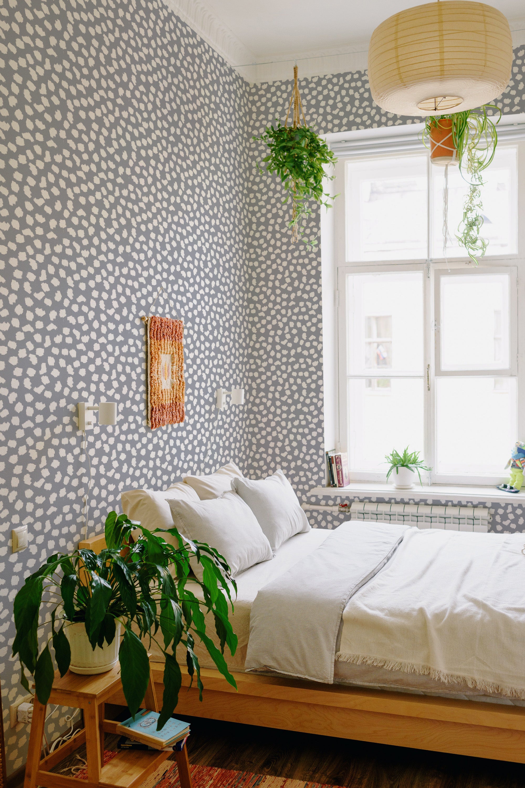 A room with walls covered in Brush dots wallpaper with an irregular pattern of white dots on a muted gray background, creating a soft and subtle texture. The wallpaper complements the minimalist decor and adds visual interest while maintaining a calm atmosphere. Traditional wallpaper.