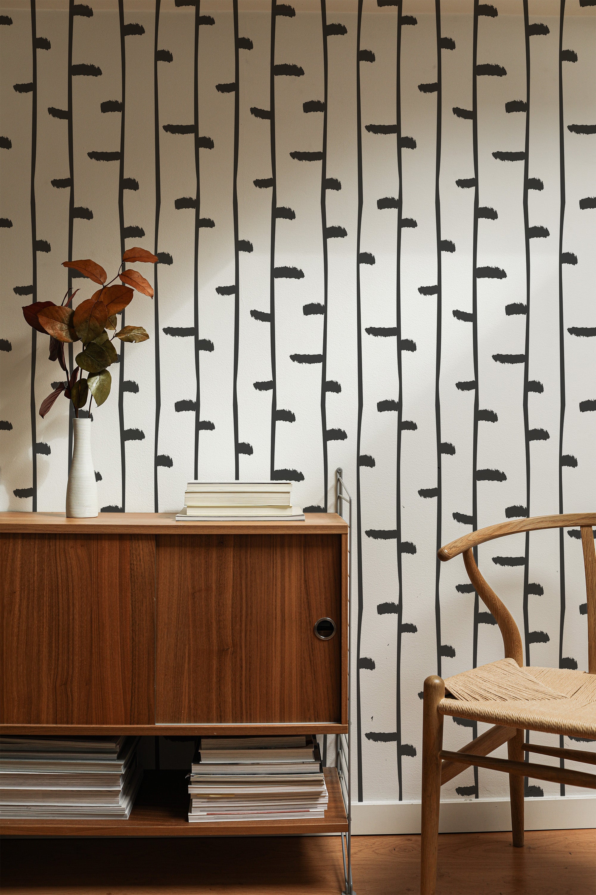 Self-adhesive wallpaper with a minimal birch tree pattern of simple vertical black lines on a white background, enhancing the room's natural and modern aesthetic.
