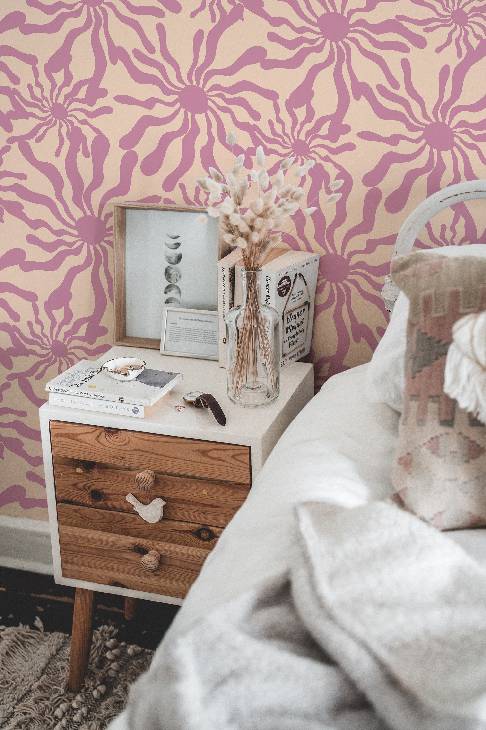 Self-adhesive wallpaper with a funky sun pattern in pink on a light beige background, adding a bold and retro touch to a cozy bedroom setting with a wooden nightstand and neutral d��cor.