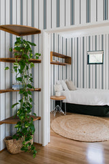 Wallpaper with vertical stripes in alternating shades of light gray and dark gray, creating a subtle and elegant pattern. The design gives a clean, timeless appearance, complementing the wooden accents and natural elements in the room. The overall style is classic and understated, emphasizing a traditional wallpaper.