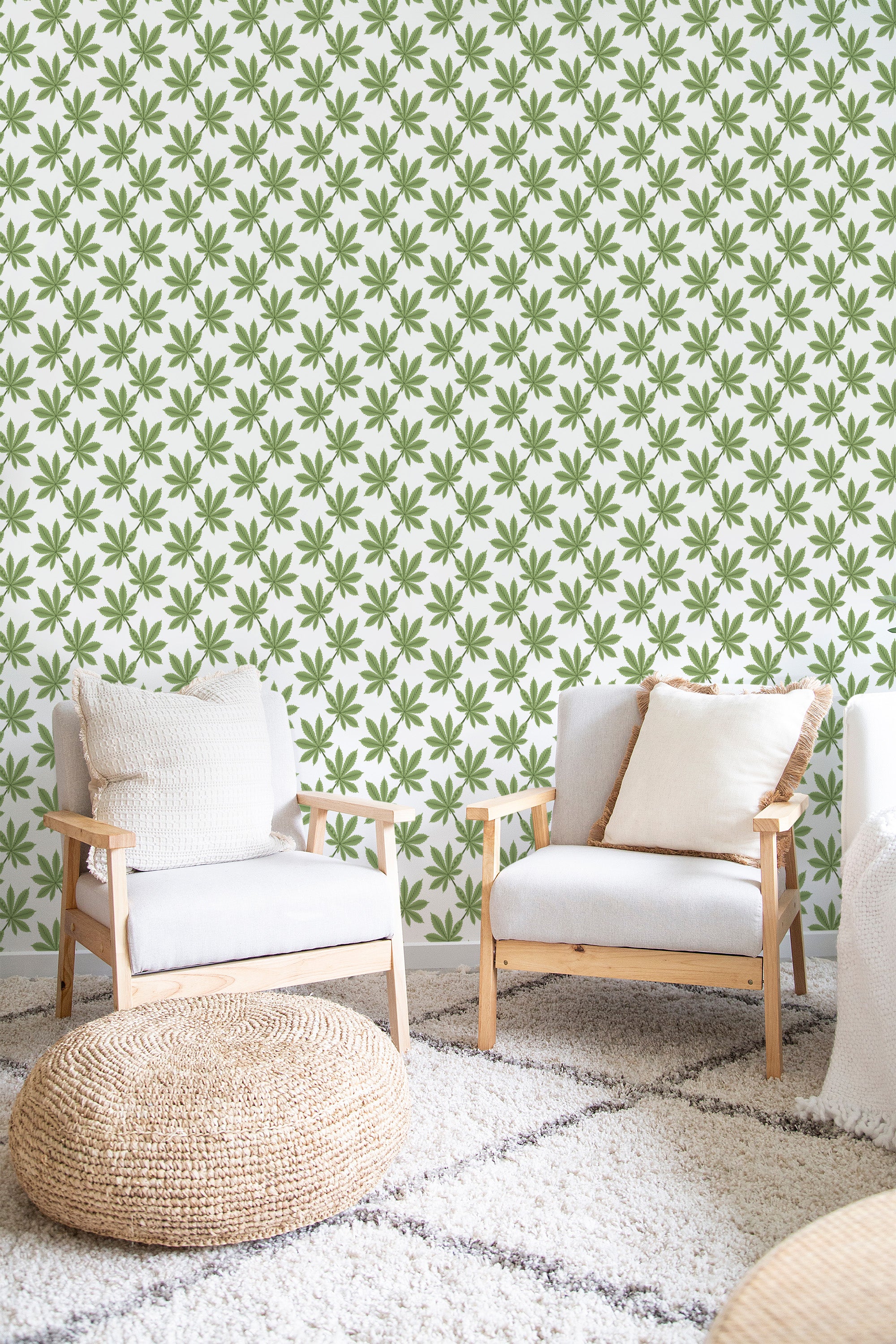 Green leaves arranged in a repetitive, symmetrical pattern on a pale background, filling the entire wall in the room. Two neutral-toned armchairs and a woven pouf sit in front, enhancing the natural aesthetic of the traditional wallpaper.