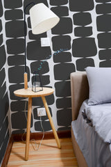 Self-adhesive wallpaper with a black retro shape design, featuring bold, organic patterns reminiscent of mid-century modern aesthetics. The graphic shapes create a striking contrast against the light-colored background, adding depth and visual interest to the space.