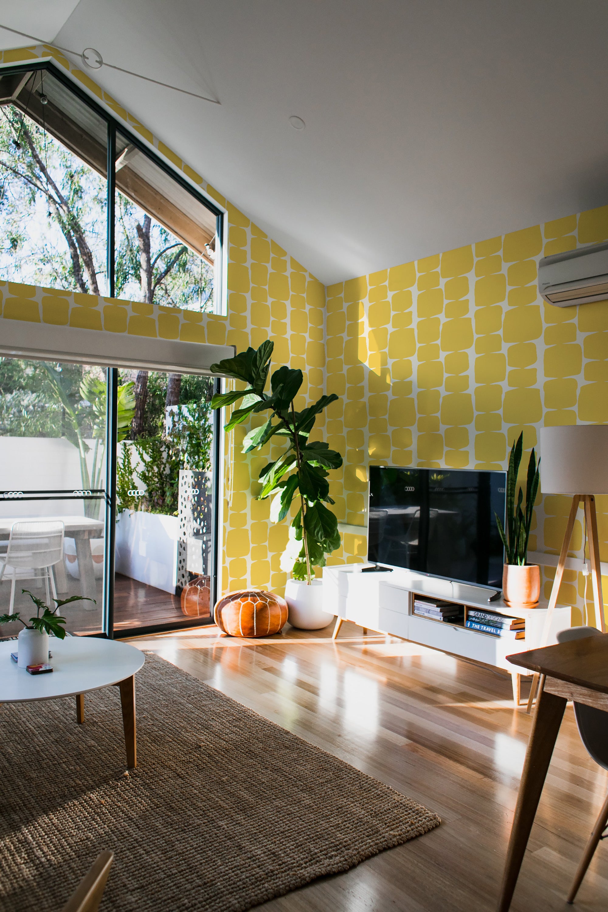 Yellow retro shape pattern wallpaper covering a living room wall in bold, geometric yellow squares and rounded shapes, creating a vibrant yet nostalgic atmosphere. Modern furnishings contrast with the traditional wallpaper.