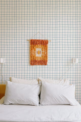 Self-adhesive wallpaper with a minimalist grid pattern in light blue lines on a white background, installed behind a bed with white pillows.