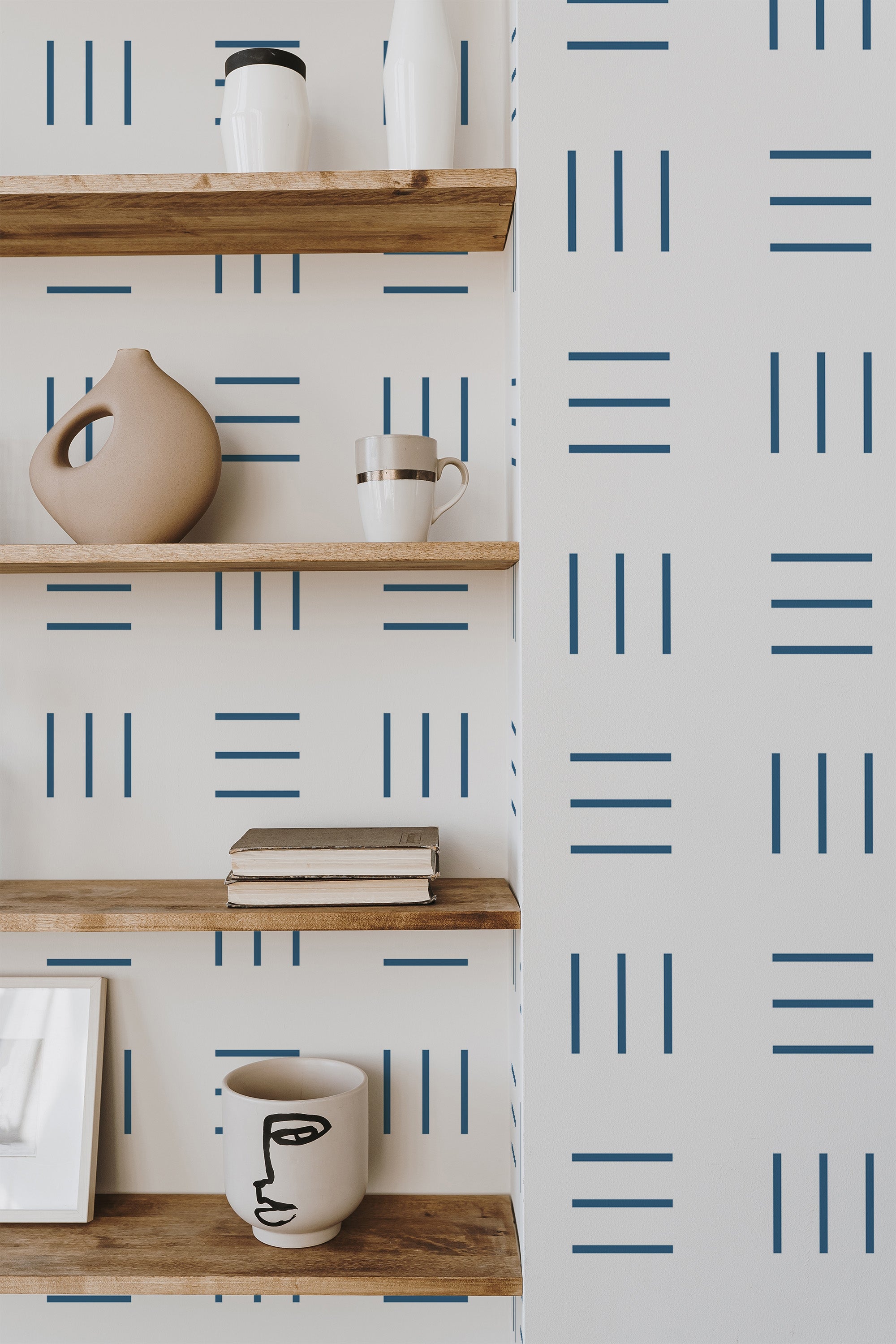 Self-adhesive wallpaper with a geometric kitchen pattern in blue lines arranged in groups of three on a white background, complementing wooden shelves with modern decor items.