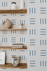 Self-adhesive wallpaper with a geometric kitchen pattern in blue lines arranged in groups of three on a white background, complementing wooden shelves with modern decor items.