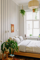 A room with wallpaper that has vertical stripes in varying shades of soft grey and cream, creating a subtle and calming contrast. The pattern adds height and elegance to the space, giving a classic, timeless feel to the room. Traditional wallpaper.
