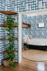 Blue and white grid-patterned wallpaper with varying line thicknesses and brushstroke textures covers the walls of a cozy room, creating a classic and elegant look. Traditional wallpaper.