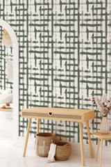 A room with green brushstroke pattern forming an abstract, imperfect grid on the wall, creating a textured and artistic effect. Complemented by a light, minimalist console table with woven baskets beneath, the wallpaper adds a modern twist to traditional wallpaper.