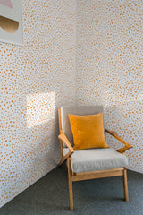 Wall covered with dotted pattern wallpaper in warm tones, featuring small, irregularly spaced dots on a light background, creating a subtle, textured look. A cozy chair with a mustard-colored cushion adds a pop of color, complementing the traditional wallpaper.