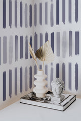 Self-adhesive wallpaper with a Brush design of vertical, paintbrush-like strokes in varying shades of grey, blue, and soft purple, creating a modern, artistic look.