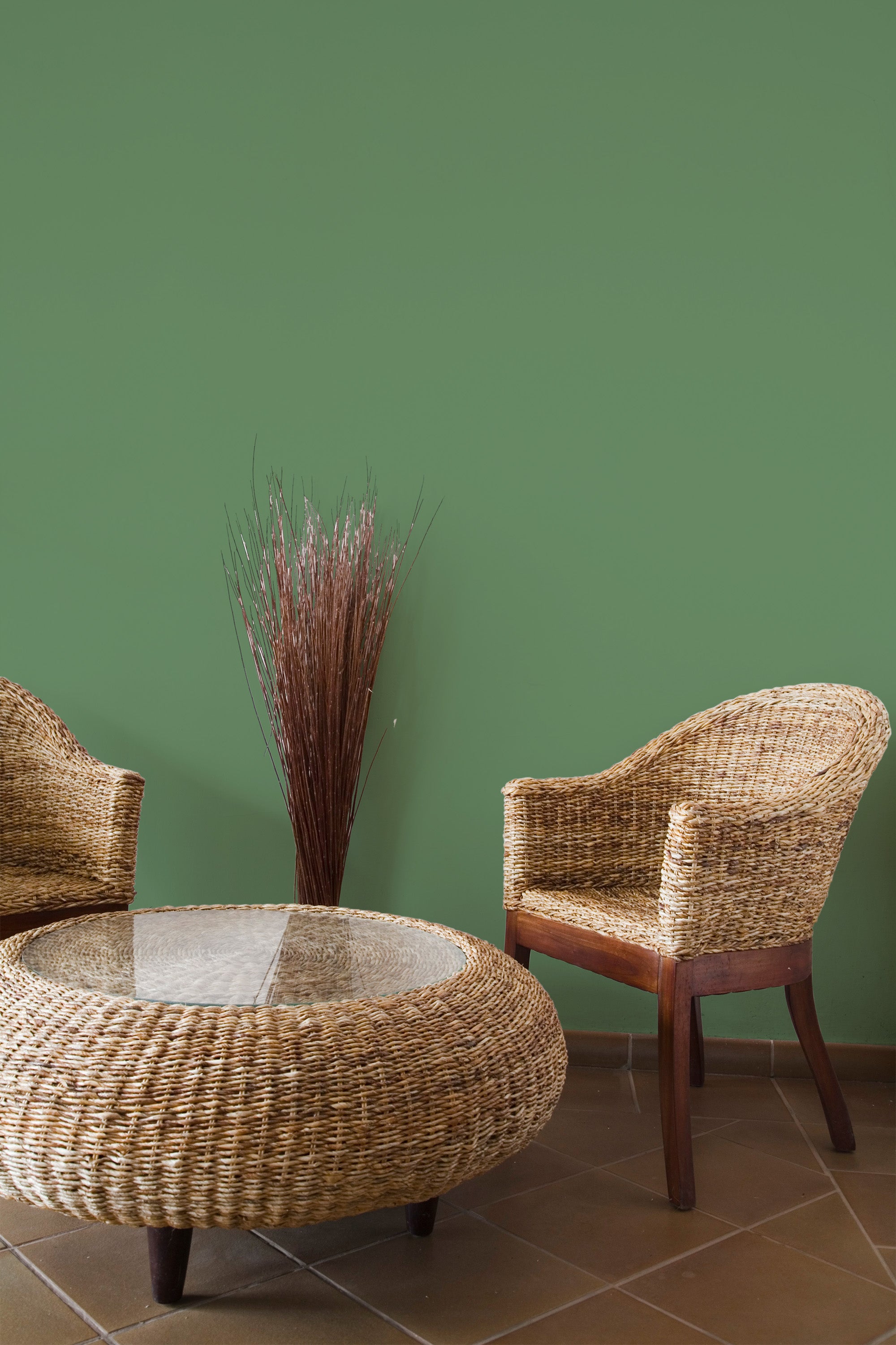 Self-adhesive solid dark green wallpaper adding a bold, smooth finish to a room with natural-toned wicker furniture and a decorative vase of sticks, creating a warm, earthy atmosphere.