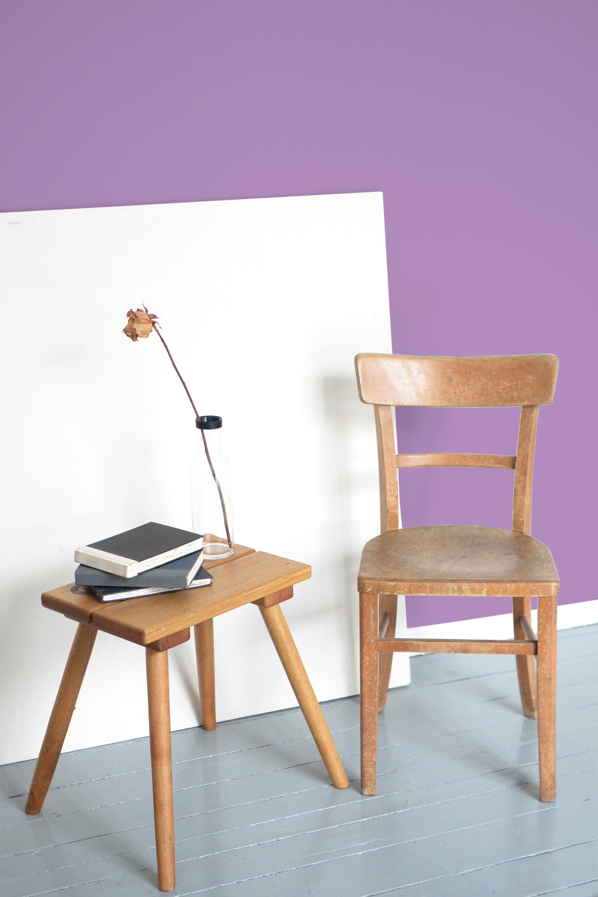 Self-adhesive solid purple wallpaper on a wall behind a wooden chair and a small wooden side table with a stack of books and a glass bottle on top.