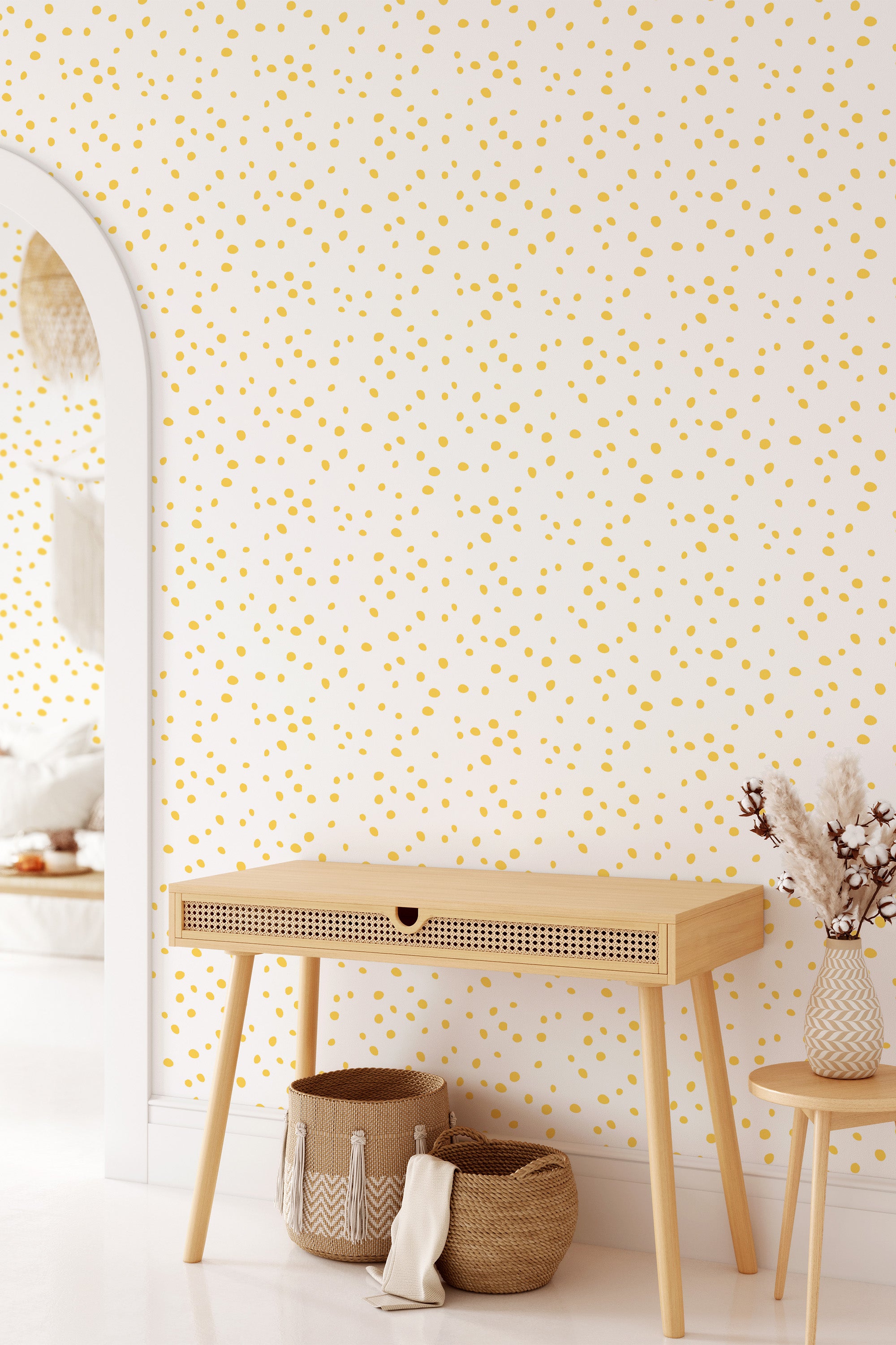 A room with a white wall covered in a Dalmatian-inspired wallpaper pattern with small, irregular golden yellow spots scattered across the surface. A light wooden desk sits against the wall, accompanied by woven baskets and decorative items. Traditional wallpaper.