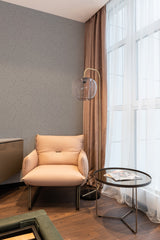 Wallpaper with a subtle, minimalist tree pattern in soft tones covers the wall of a cozy room with a contemporary chair, side table, and soft lighting,raditional wallpaper.